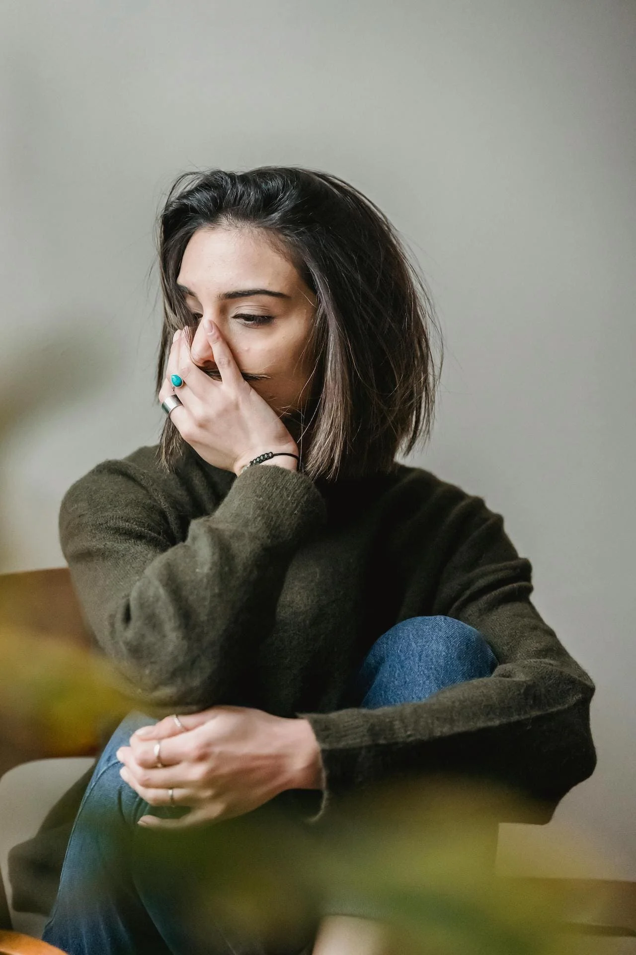 femme assisse en vert recrocvier sur elle même la main sur la bouche souffrant d'endométriose